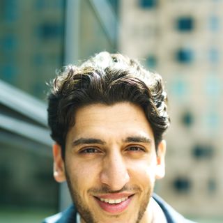 A man in his thirties smiling on a city street.