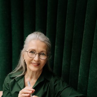 A woman in her sixties wearing glasses, smiling.