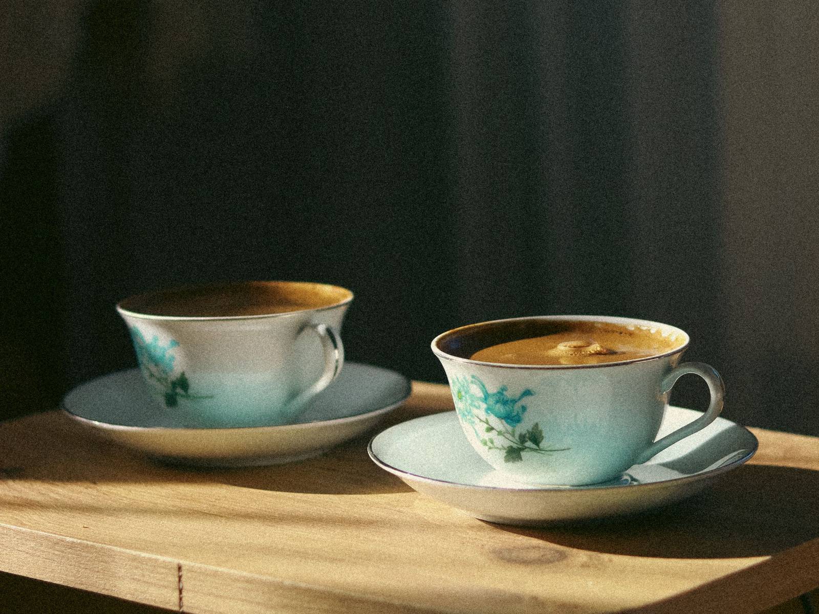 Two mugs and an open notepad on a timber dining table in late afternoon light.