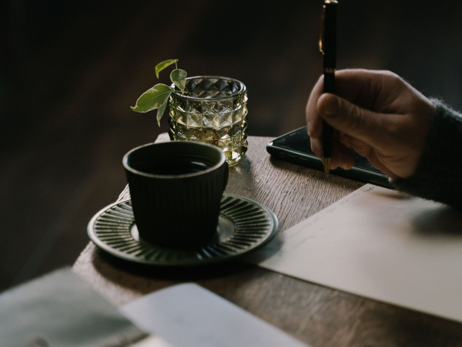 Two pairs of hands and a coffee cup resting either side of a single sheet of paper on a kitchen table.